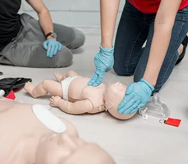 Chest compressions on a baby dummy during the first aid training indoors